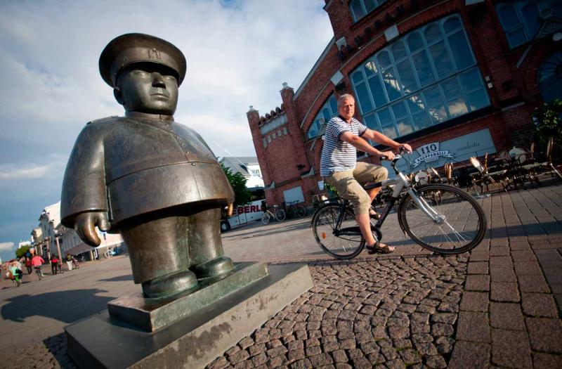 A statue of Toripolliisi and a cyclist in front of Kauppahalli in Oulu.